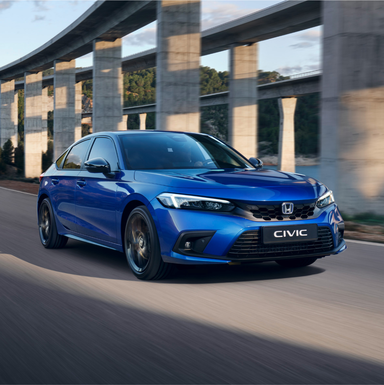 Modrý hybrid Civic idúci v horskej krajine.