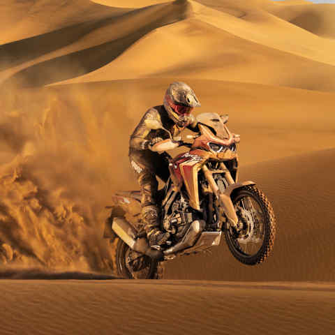 Trojštvrťový pohľad spredu z pracej strany na model Honda CRF1100L Africa Twin, jazda na zašpinenom motocykli v piesku