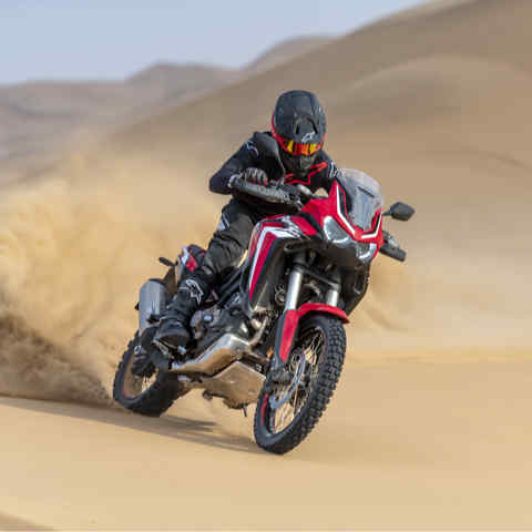 Trojštvrťový predný záber z pravej strany na model Honda Africa Twin, jazda na čistom motocykli v piesku
