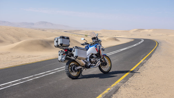 Trojštvrťový záber zhora z ľavej strany na model Honda Africa Twin Adventure Sports pri jazde po ceste v púšti
